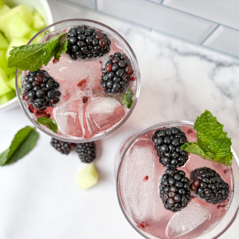 Birds eye view of two honeydew watermelon mocktails sitting diagonal to each other with garnishes and melon in the background