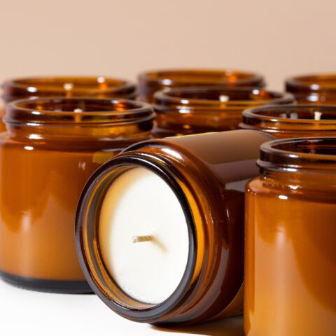 Rows of candles in glass amber jars, with one candle tipped on its side to show the wick