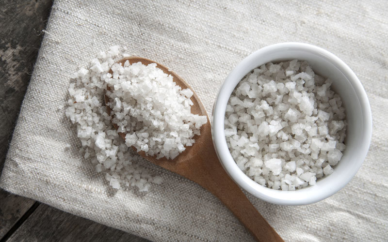 Celtic sea salt in a bowl and on a wooden spoon on a table cloth.