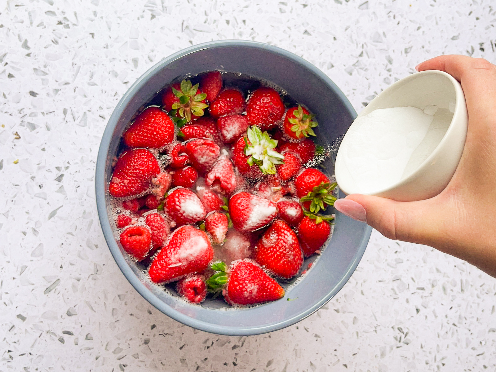 Baking soda being poured on berries in a bowl