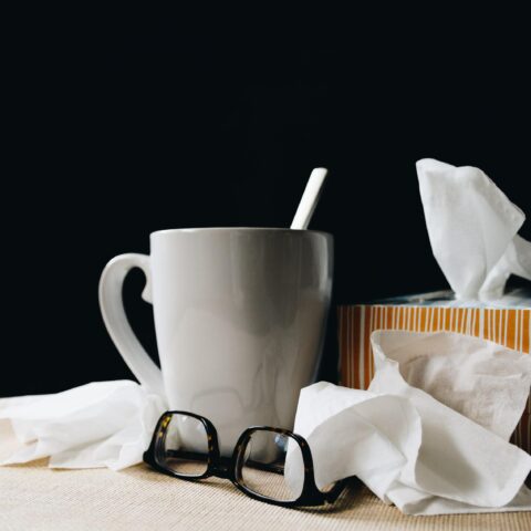 A box of tissues, a hot drink and a pair of reading glasses.