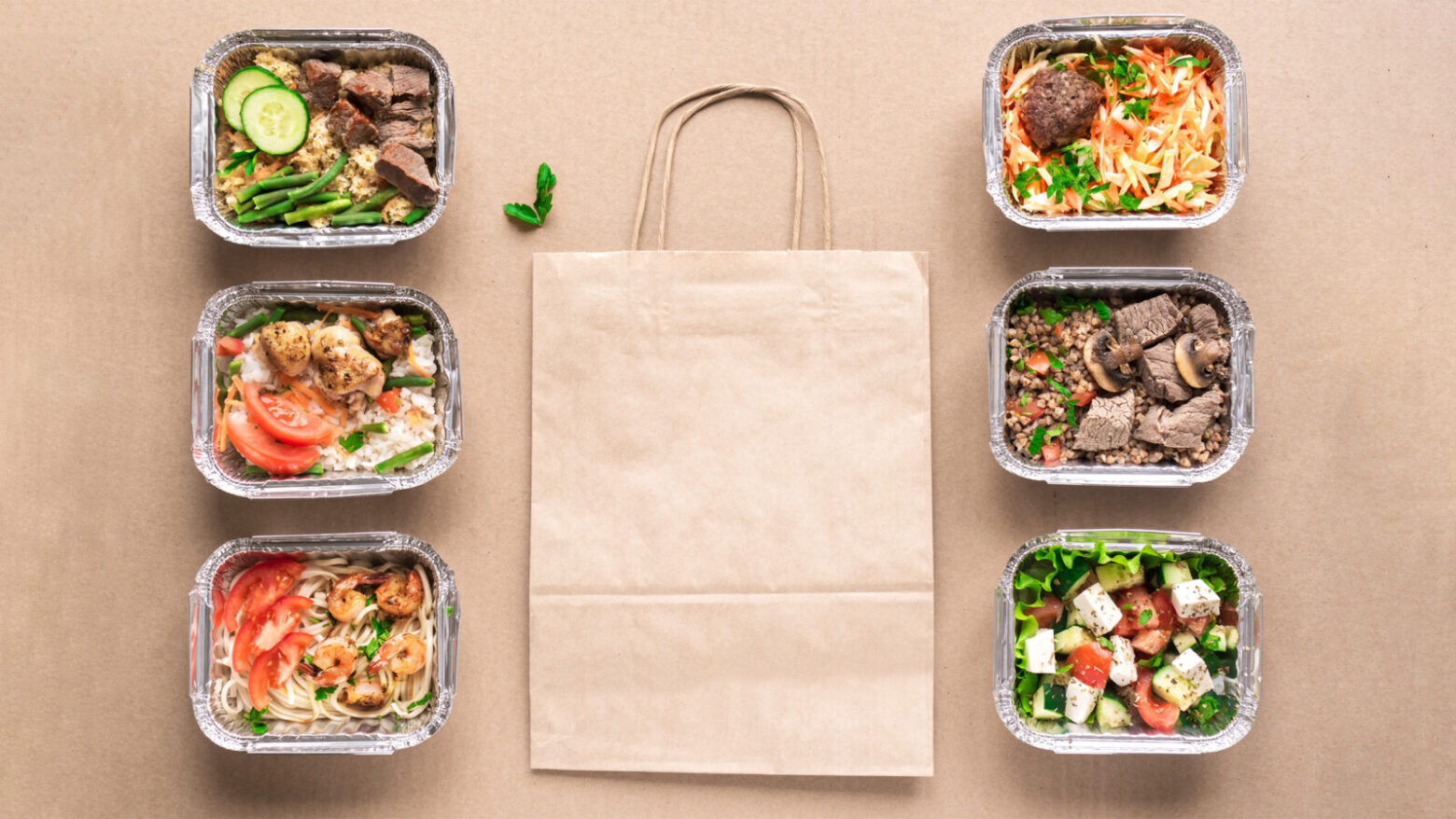 Above shot of different Paleo takeout meals in trays with a paper bag.