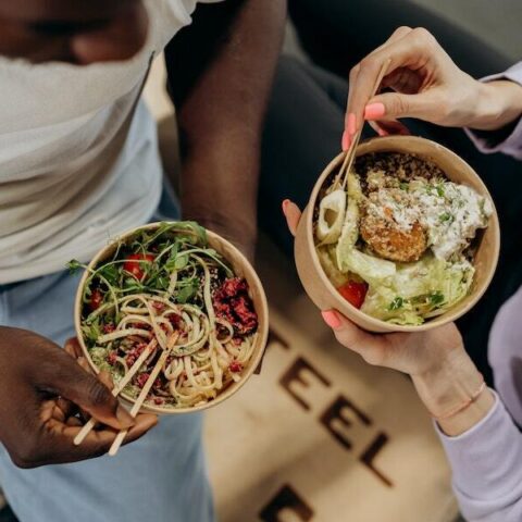 Two people each eating food from a bowl using chopsticks.