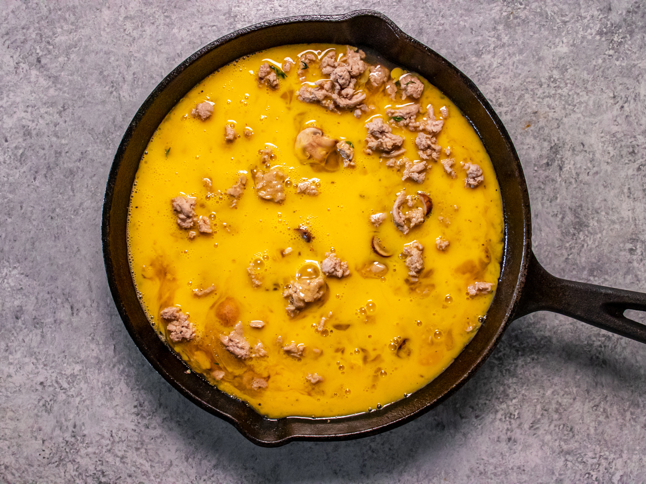 Protein-packed mushroom frittata prepped in a pan with raw egg, mushrooms, and ground meat. 