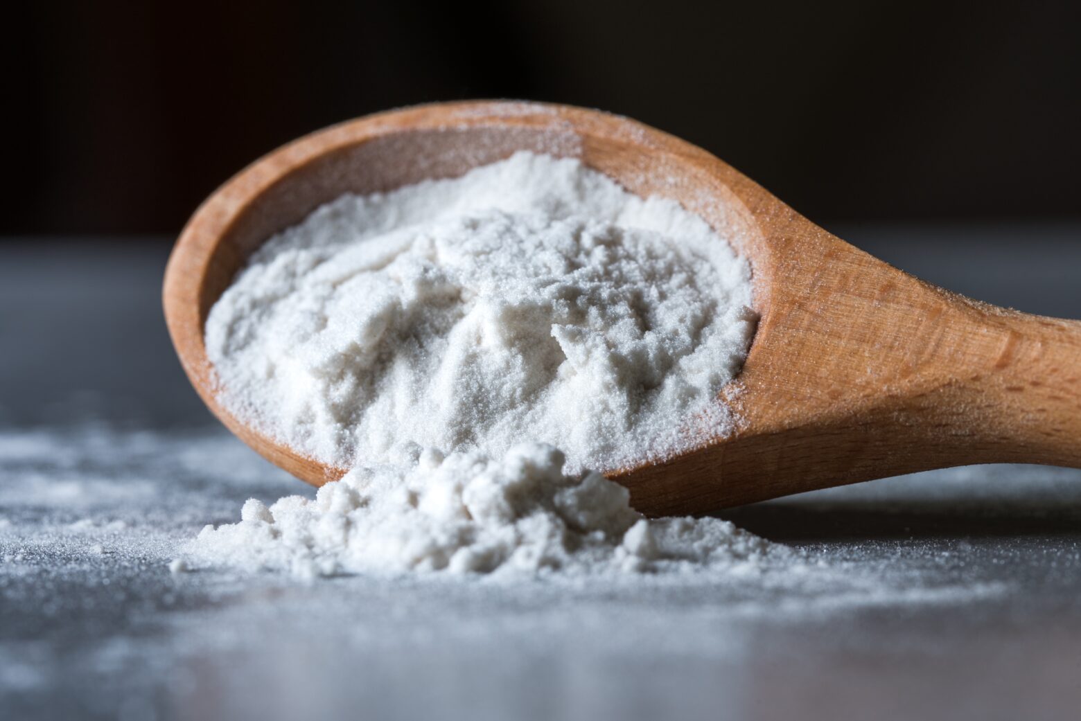 A wooden spoon spills tapioca flour onto a table.