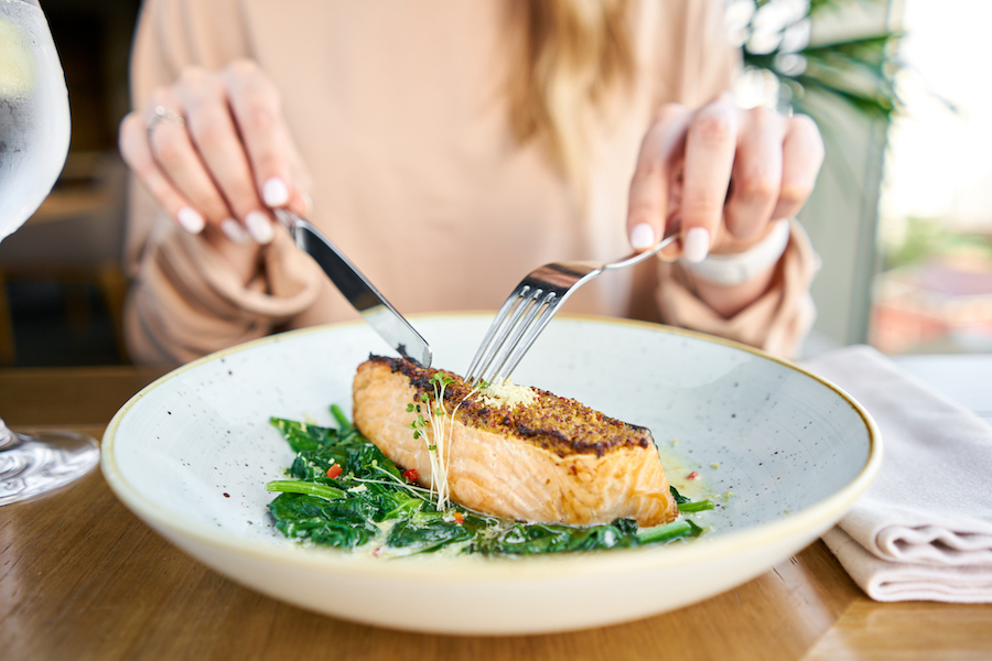 A woman cuts some fish in a bowl at a dinner table.