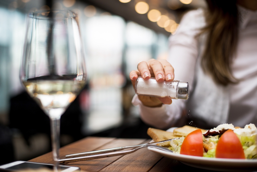 Is salt Paleo? A woman adds salt to a dish at a restaurant.