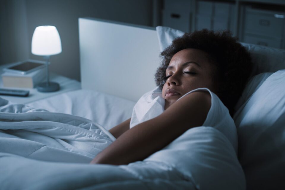 Woman sleeping in bed with small light on nightstand.