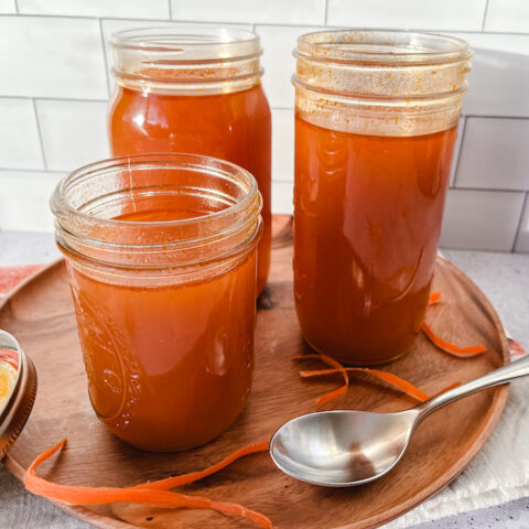 Three mason jars containing vegetable broth on a wooden tray with a silver spoon.