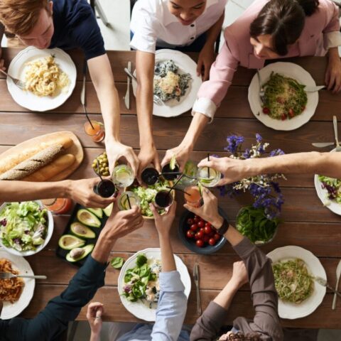 A group of people cheers over a dining table full of food.