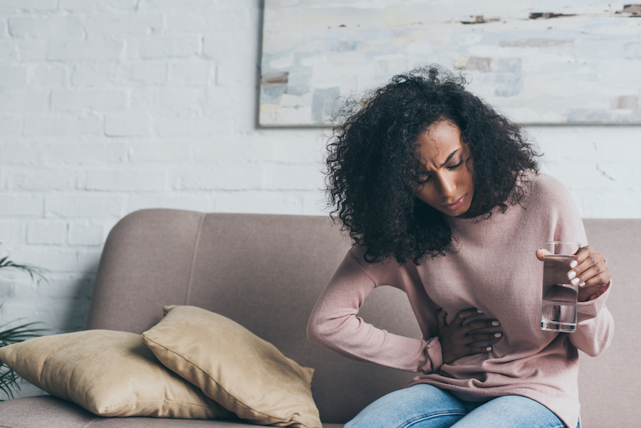 A woman in pain sitting on a couch with her hand on her stomach.